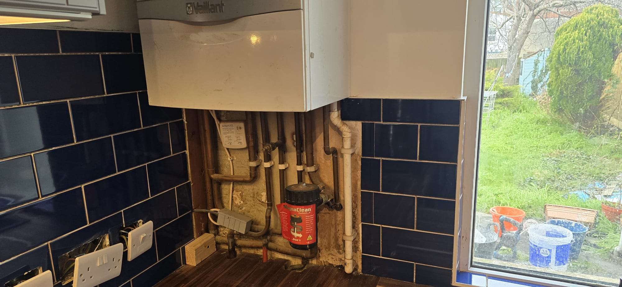 Exposed under-boiler pipework including flow, return, gas, cold feed, hot water, and condensate pipes in a kitchen before covering